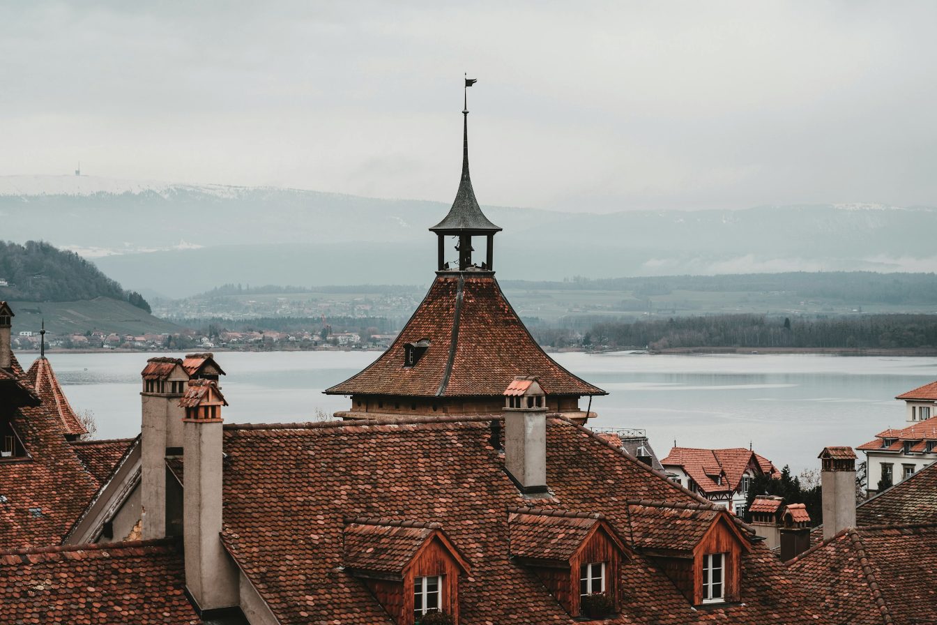 Tiled rooftops of an old town with a tower, the lake and the Jura behind